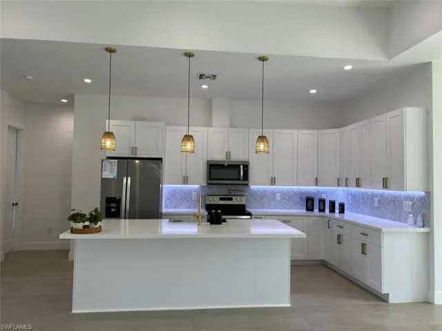 Kitchen with appliances with stainless steel finishes, tasteful backsplash, decorative light fixtures, a kitchen island with sink, and white cabinetry