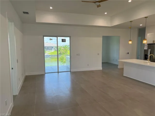 Unfurnished living room featuring a tray ceiling, tile flooring, sink, and ceiling fan