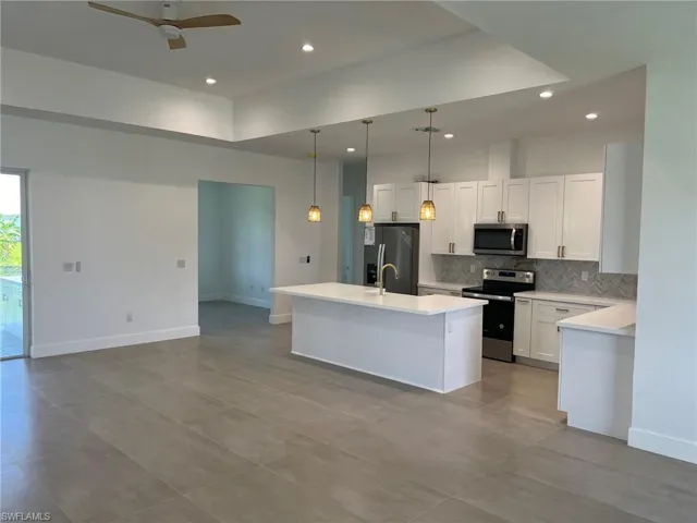 Kitchen featuring white cabinetry, stainless steel appliances, an island with sink, decorative light fixtures, and ceiling fan