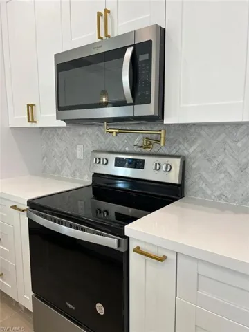 Kitchen featuring appliances with stainless steel finishes, white cabinets, and backsplash