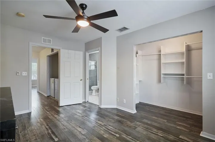 Unfurnished bedroom featuring dark wood-style floors, washer and clothes dryer, visible vents, and baseboards