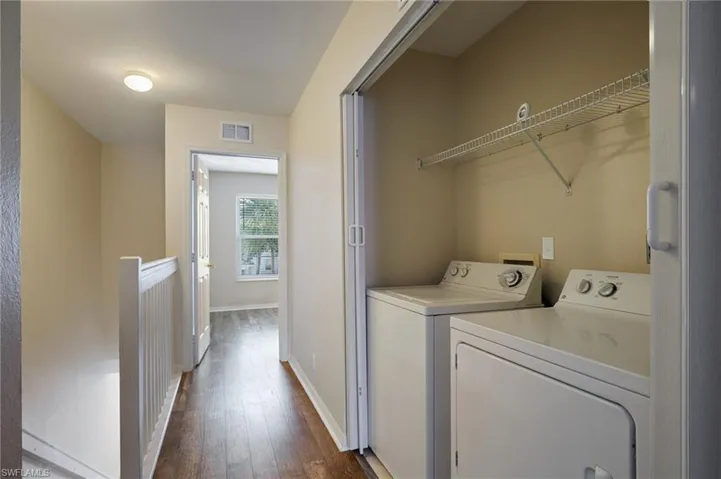 Laundry room with dark wood finished floors, washing machine and clothes dryer, visible vents, laundry area, and baseboards