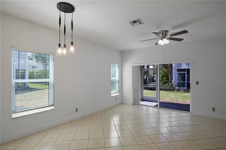 Tiled spare room featuring ceiling fan with notable chandelier, visible vents, and baseboards