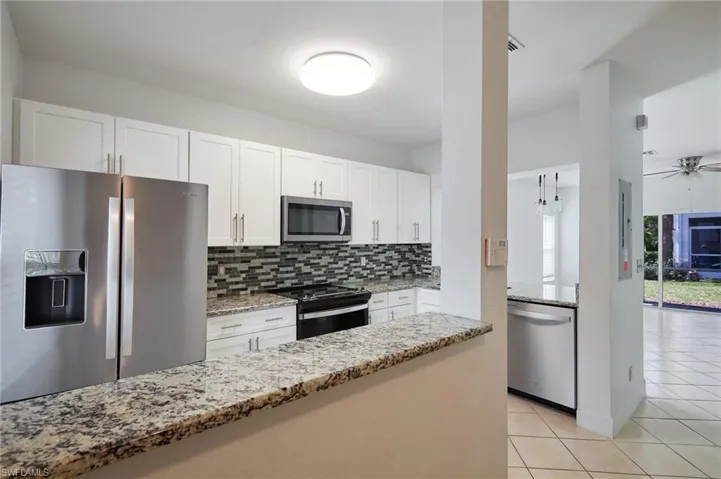 Kitchen featuring appliances with stainless steel finishes, white cabinetry, light stone countertops, and tasteful backsplash