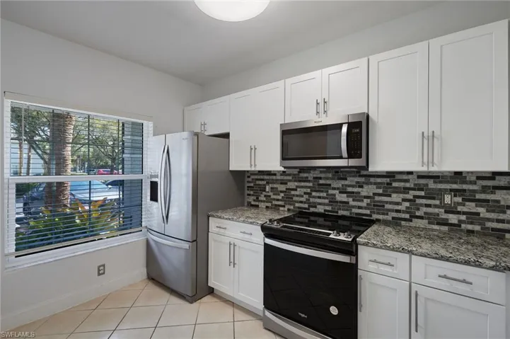Kitchen with light tile patterned floors, stainless steel appliances, tasteful backsplash, and white cabinetry