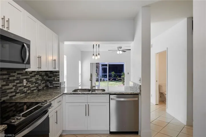 Kitchen with light stone counters, a sink, stainless steel appliances, white cabinetry, and backsplash