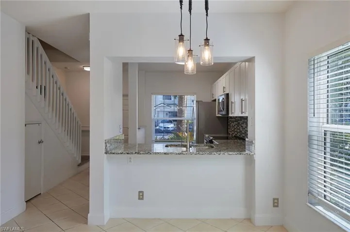 Kitchen with stainless steel microwave, decorative backsplash, white cabinetry, and light stone countertops