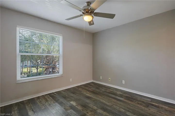 Empty room with dark wood finished floors, a ceiling fan, and baseboards
