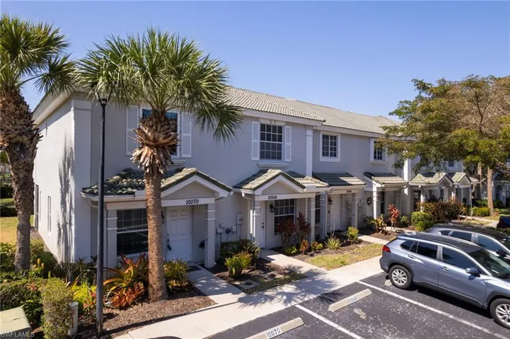 View of property with stucco siding, uncovered parking, and a tiled roof
