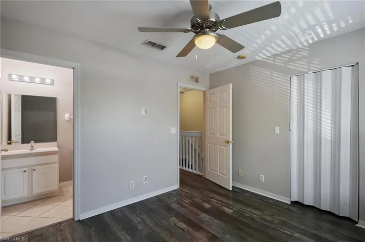 Unfurnished bedroom with visible vents, ensuite bath, baseboards, and wood finished floors