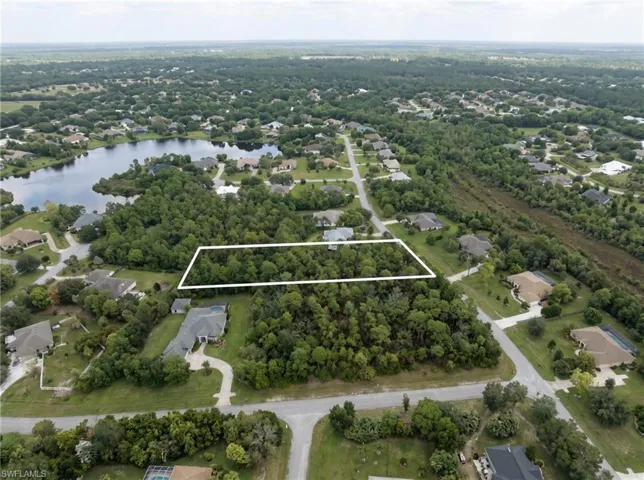 Expansive lot with mature trees, surrounded by residential properties and a nearby body of water