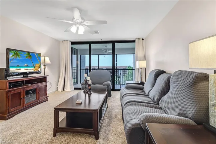 Carpeted living room with floor to ceiling windows and ceiling fan