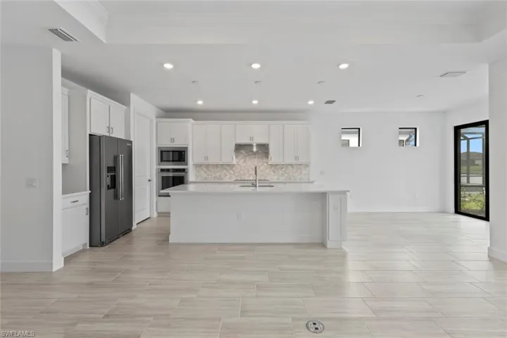 Kitchen featuring white cabinets, stainless steel appliances, an island with sink, recessed lighting, and tasteful backsplash