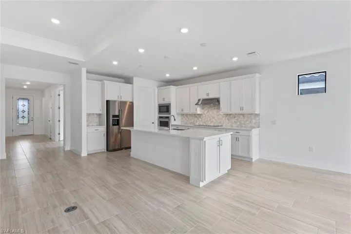 Kitchen featuring white cabinets, decorative backsplash, stainless steel appliances, a kitchen island with sink, and plenty of natural light