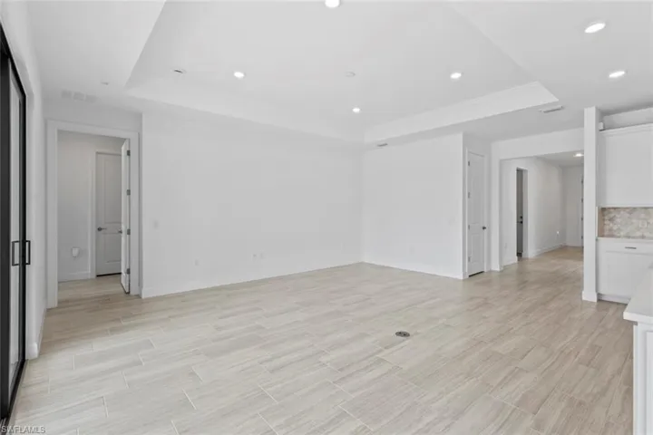 Empty room with a tray ceiling, wood finish floors, and recessed lighting