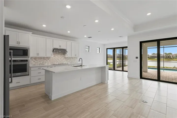 Kitchen with white cabinets, an island with sink, stainless steel appliances, tasteful backsplash, and light stone counters