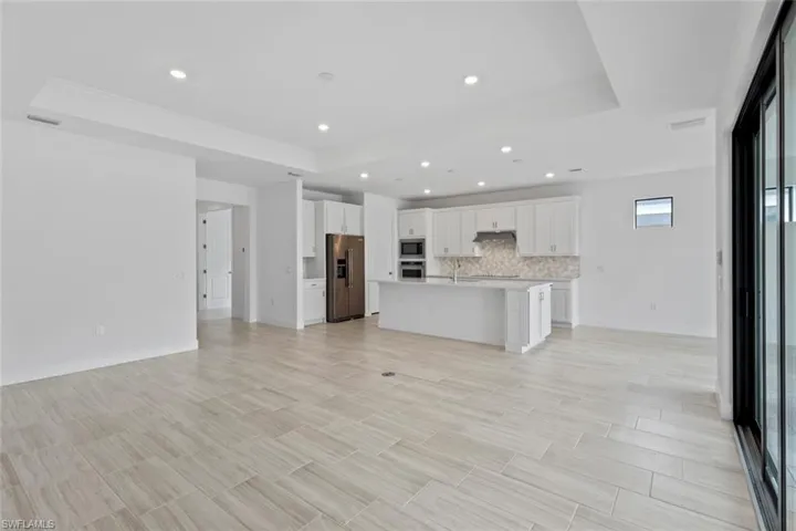 Kitchen with white cabinetry, a raised ceiling, a kitchen island with sink, stainless steel appliances, and open floor plan