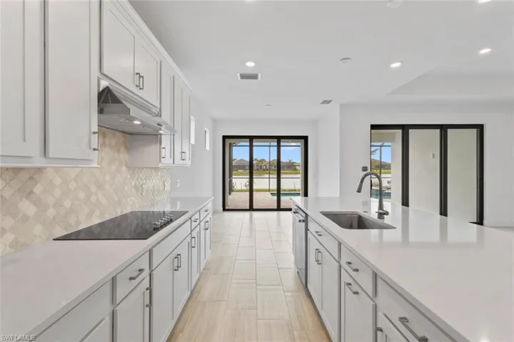 Kitchen with recessed lighting, light stone countertops, black electric stovetop, and white cabinets