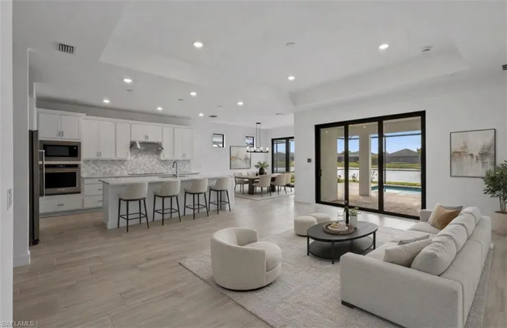 Digitally staged** Living area featuring light wood finished floors, a raised ceiling, and recessed lighting