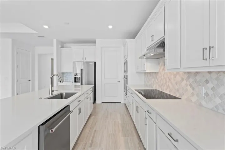 Kitchen with white cabinets, stainless steel appliances, recessed lighting, light stone countertops, and tasteful backsplash