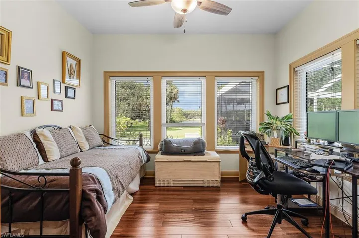 Bedroom with multiple windows, a desk, dark wood-style flooring, and ceiling fan