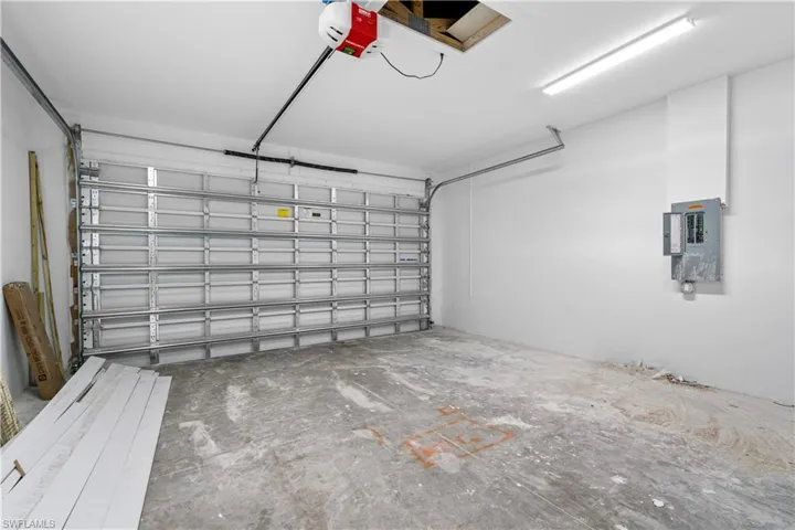 Spacious garage featuring an overhead garage door, concrete flooring, overhead fluorescent lighting, and an exposed electrical panel