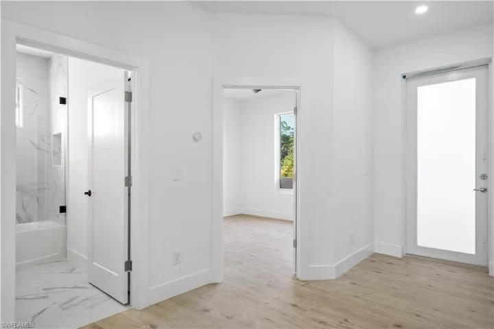 Hallway area featuring wood-finish flooring, a contemporary white door with a frosted glass panel, and recessed lighting