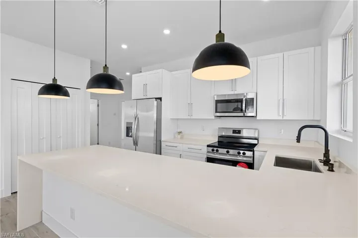 Kitchen featuring an expansive island with a built-in sink, white cabinetry, stainless steel appliances, and pendant lighting