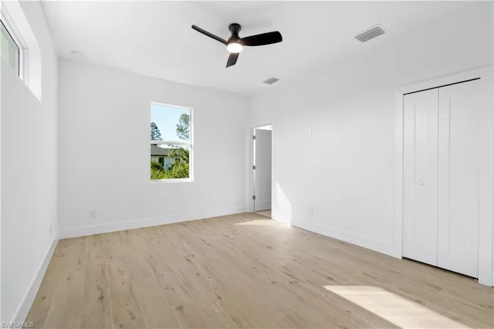Bright room featuring light wood-finish flooring, a contemporary ceiling fan with integrated lighting, and white walls