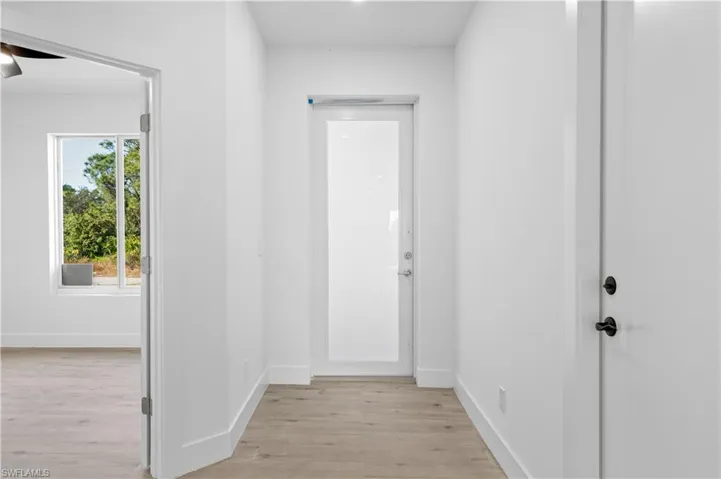 Entryway featuring light wood-finish flooring, white walls, a full-light panel door, and a solid interior door with matte black hardware