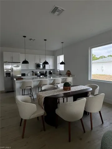 Open-concept kitchen and dining area featuring white cabinetry, stainless steel appliances, a kitchen island with seating, pendant lighting, and wood-finish flooring
