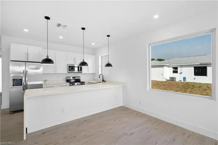 Modern kitchen featuring white shaker cabinetry, stainless steel appliances, a breakfast bar with pendant lighting, and wood-finish flooring