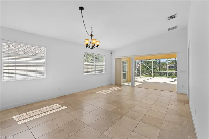 Tiled empty room featuring a chandelier and vaulted ceiling