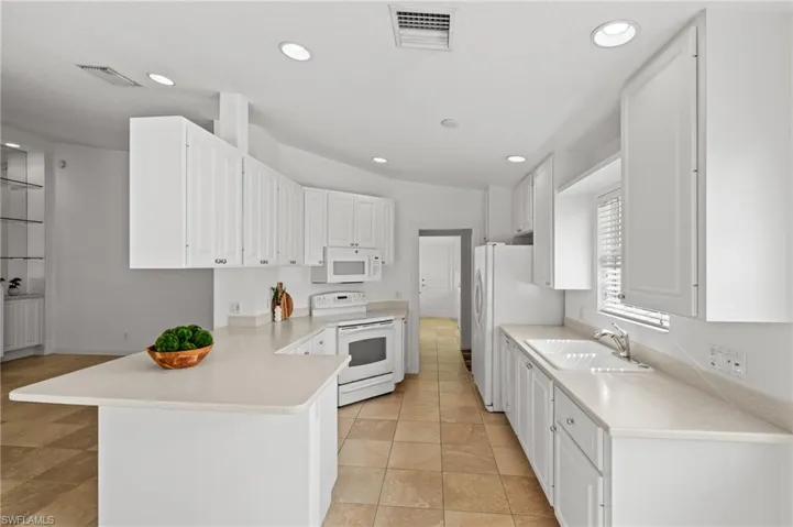 Kitchen with white cabinetry, white appliances, kitchen peninsula, and sink