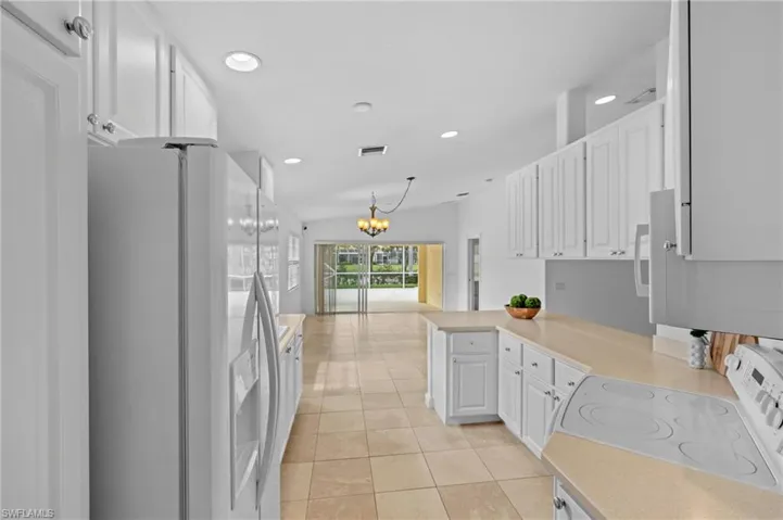 Kitchen with white cabinetry, white refrigerator with ice dispenser, light tile patterned floors, electric range, and kitchen peninsula