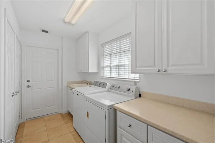 Laundry area featuring cabinets, separate washer and dryer, sink, and light tile patterned floors