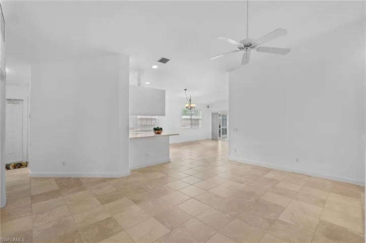 Unfurnished living room with lofted ceiling, light tile patterned floors, and ceiling fan with notable chandelier