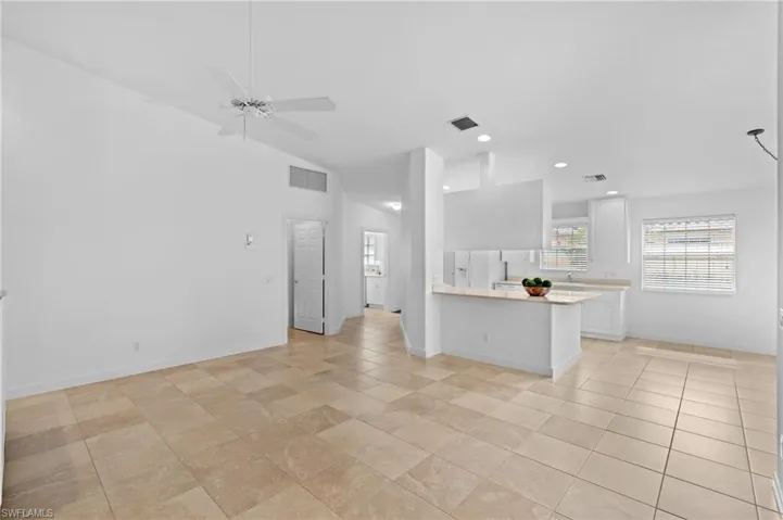 Kitchen with lofted ceiling, light tile patterned floors, ceiling fan, white cabinets, and kitchen peninsula