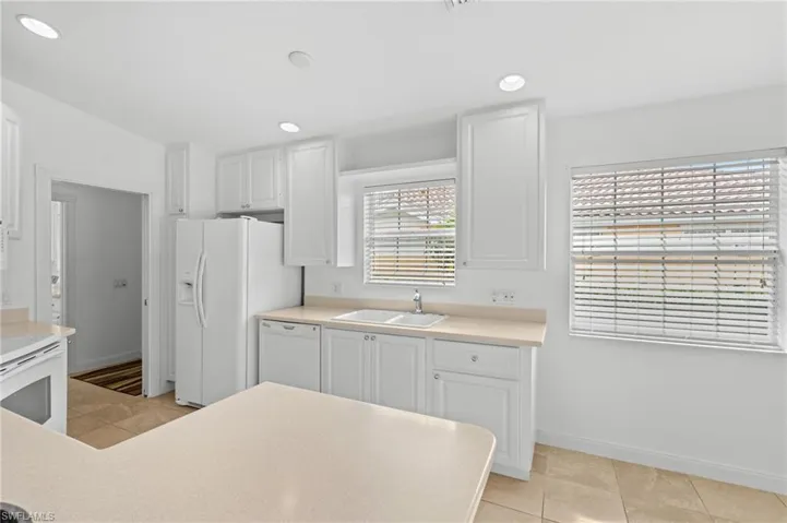 Kitchen with lofted ceiling, sink, white cabinetry, light tile patterned floors, and white appliances