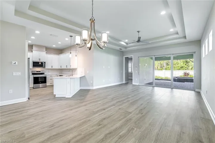 Unfurnished living room with a chandelier, a raised ceiling, light wood-style floors, a ceiling fan, and recessed lighting