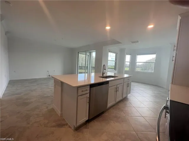 Kitchen featuring dishwasher, a sink, open floor plan, light countertops, and a center island with sink