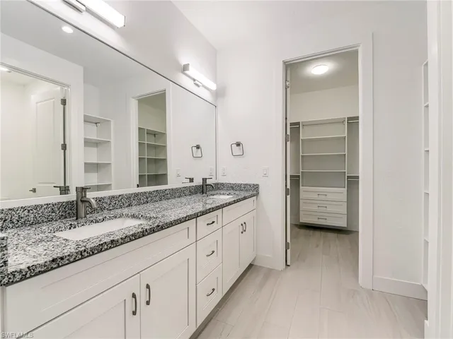 Full bath with a walk in closet, double vanity, and light wood-style flooring