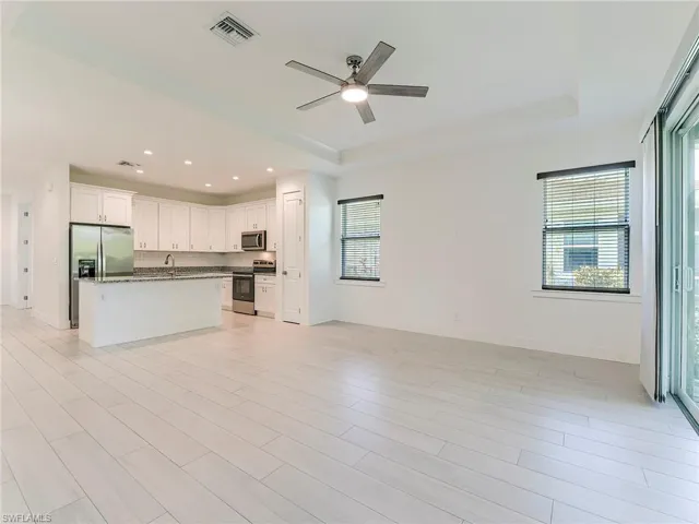 Living room open concept to Kitchen featuring open floor plan, white cabinetry, stainless steel appliances, wood tiled floors, and a raised ceiling