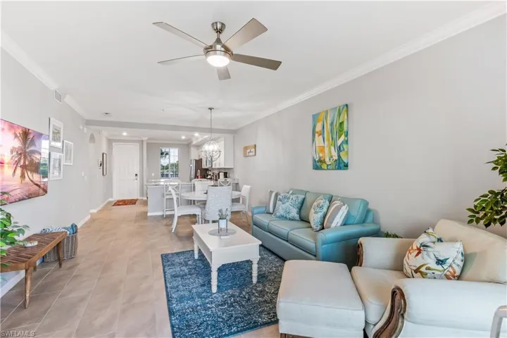 Tiled living room with crown molding and ceiling fan with notable chandelier