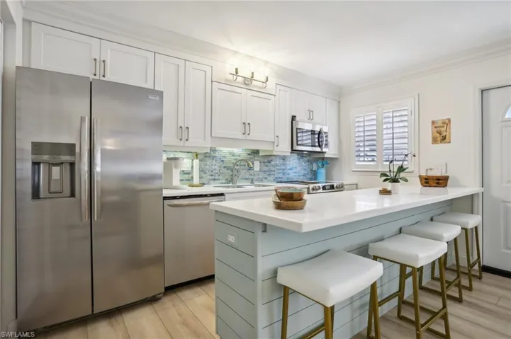 Kitchen featuring light hardwood / wood-style floors, appliances with stainless steel finishes, white cabinets, backsplash, and a breakfast bar