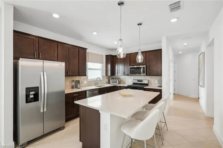 Kitchen featuring hanging light fixtures, stainless steel appliances, a breakfast bar area, dark brown cabinets, and a kitchen island