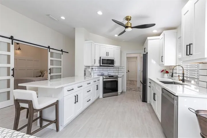Kitchen featuring a peninsula, light stone countertops, a barn door, appliances with stainless steel finishes, and recessed lighting