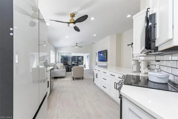Kitchen with tasteful backsplash, white cabinets, open floor plan, vaulted ceiling, and stainless steel electric range
