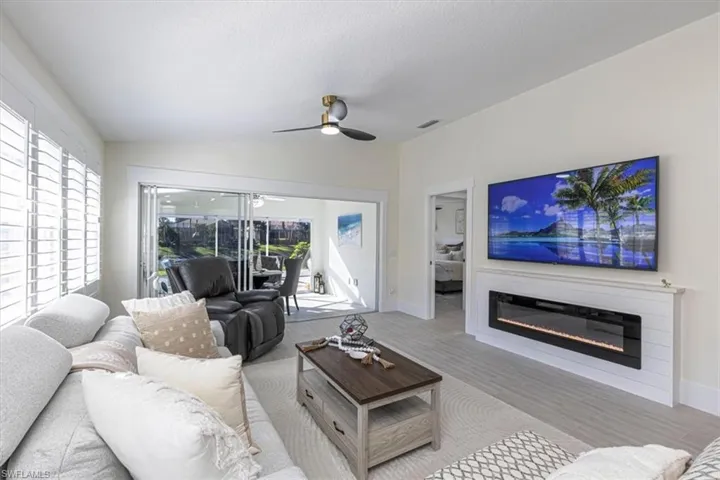 Living room featuring wood finished floors, lofted ceiling, ceiling fan, a glass covered fireplace, and a textured ceiling