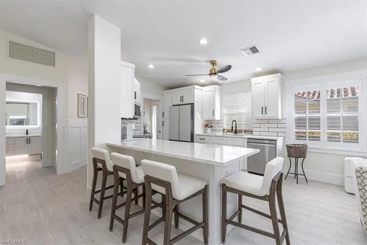 Kitchen featuring a peninsula, a breakfast bar, light stone countertops, appliances with stainless steel finishes, and white cabinets
